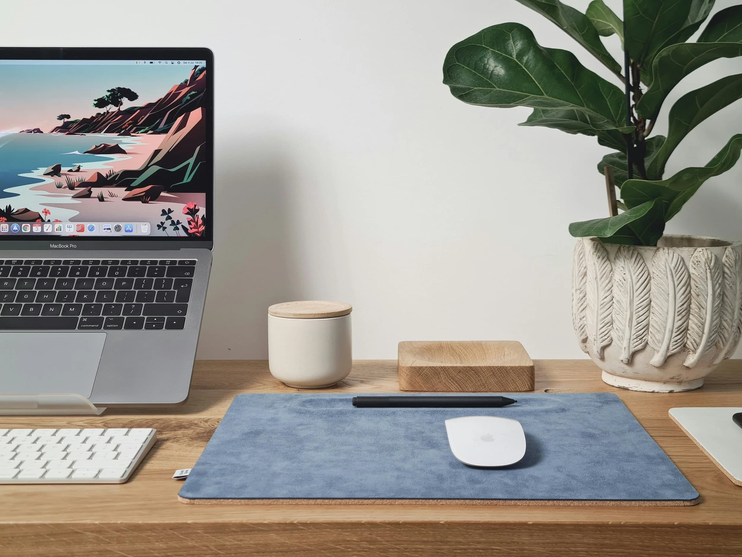 A laptop, keyboard and potted plant on a wooden desk